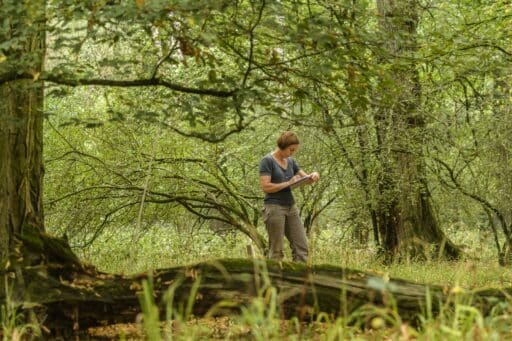 A woman writes on a pad and stands in the forest.