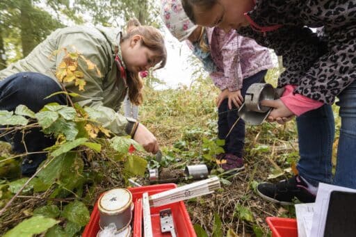 Two children and a scientist take soil samples and examine them using soil science materials.