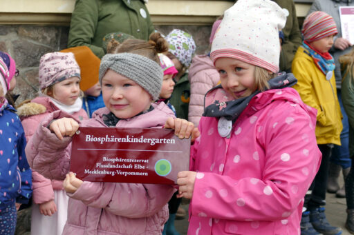 Children hold up the Biosphere Kindergarten badge.