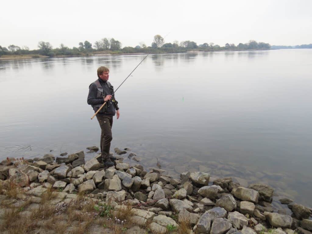 Ein Angler steht mit seiner Angel an der Elbe.