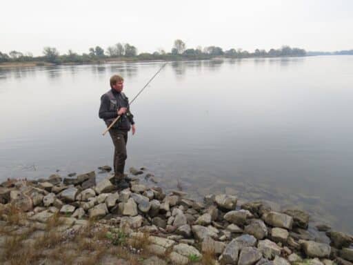 An angler stands with his fishing rod on the Elbe.