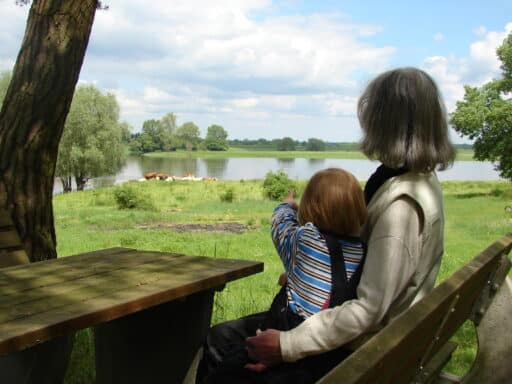 A mother and child take a picnic break at a table with a bench and look out over the Elbe.