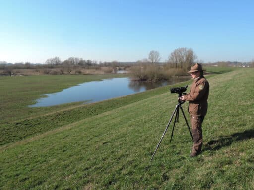 From the dyke, resting birds are observed by a ranger with a spotting scope.